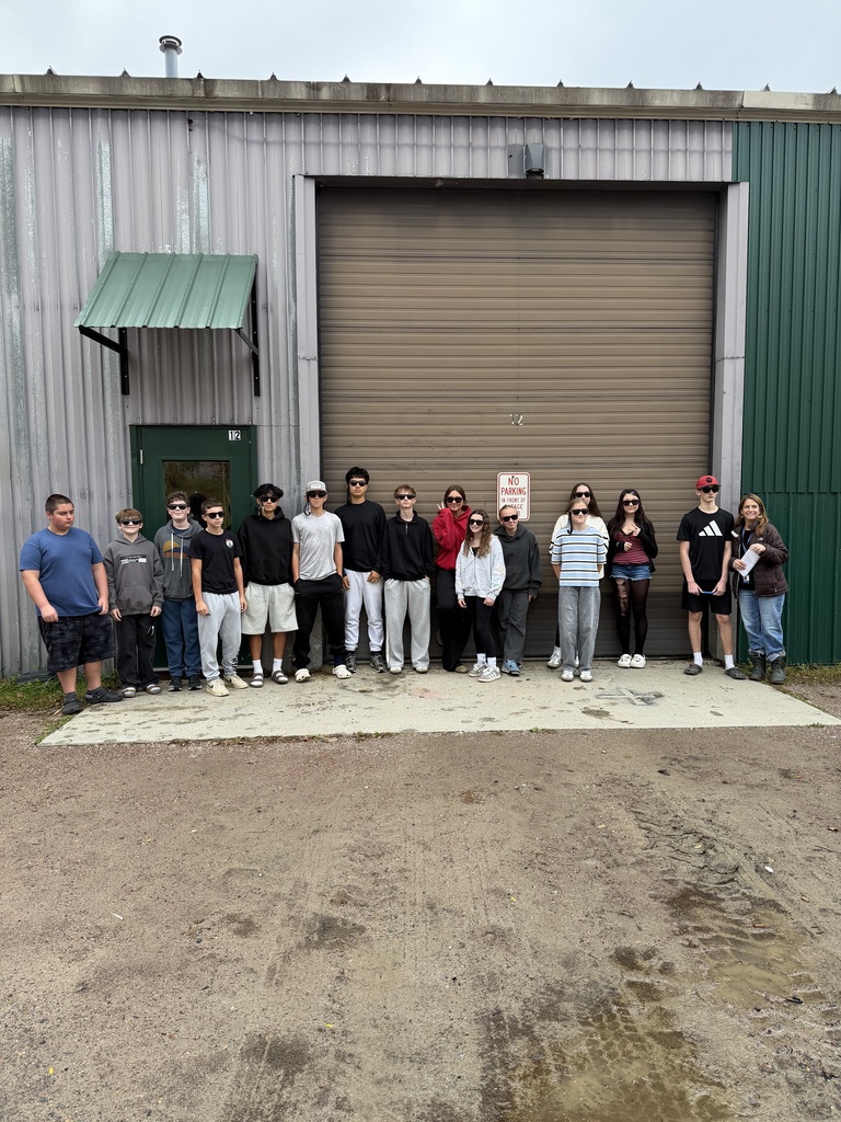 A group of people stand outside a building with a large garage door and green awning.