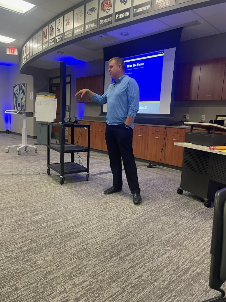 Man in a light blue long sleeved shirt presenting in front of a screen