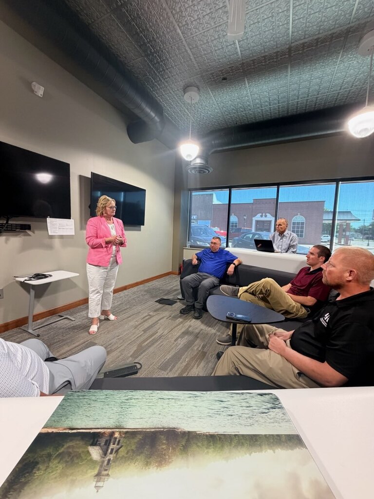 Women in pink blazer presenting to 4 men sitting in a conference room