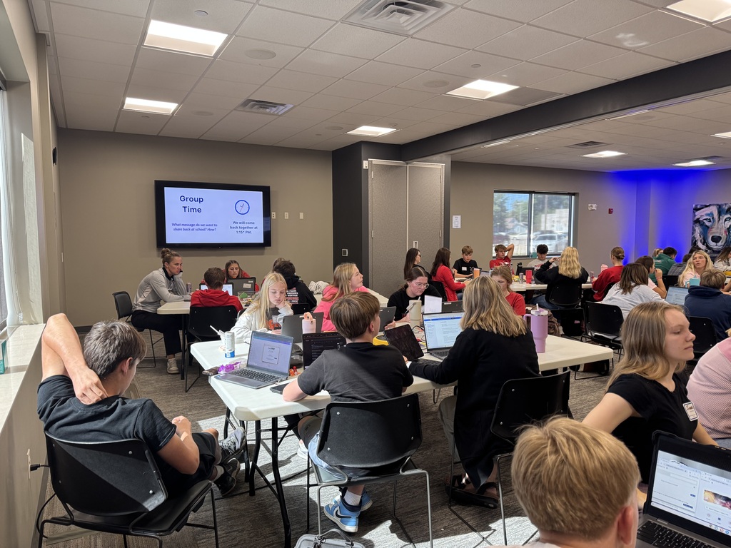 area students sit at white conference room tables and have laptops open