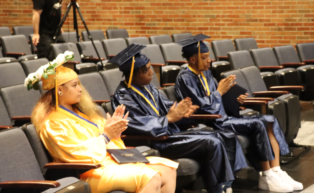 Three Euclid High School graduates wearing their graduation gowns clapping.