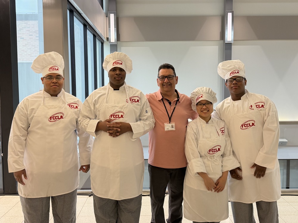 Euclid High School Culinary Arts students in chef uniforms stand with their instructor, posing together after competing in FCCLA events.