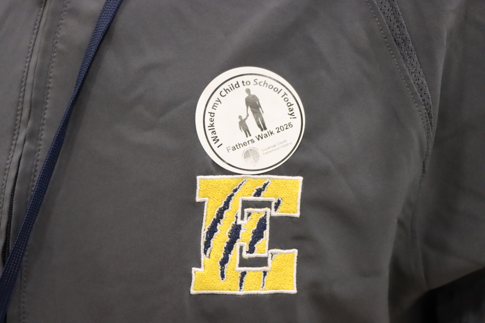 Close-up of a Fathers Walk 2026 sticker reading, “I Walked my Child to School Today!” above an embroidered gold Euclid E with navy claw marks on a gray jacket.