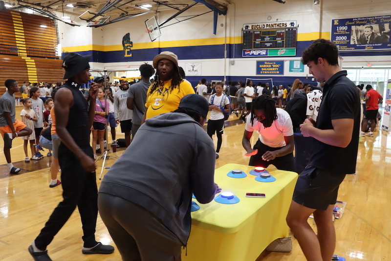 Football players test their reaction times by quickly tapping illuminated buttons while other attendees explore stations throughout the gym.