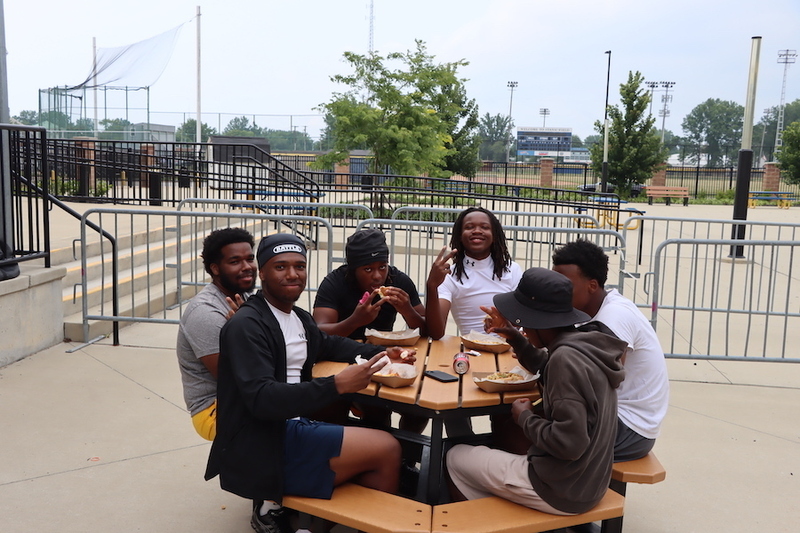 Football players sitting at an outdoor picnic table while enjoying a snack.