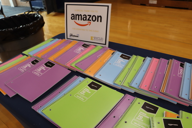 Multi-colored notebooks sitting on a table with a sign noting that Amazon donated school supplies for the event.