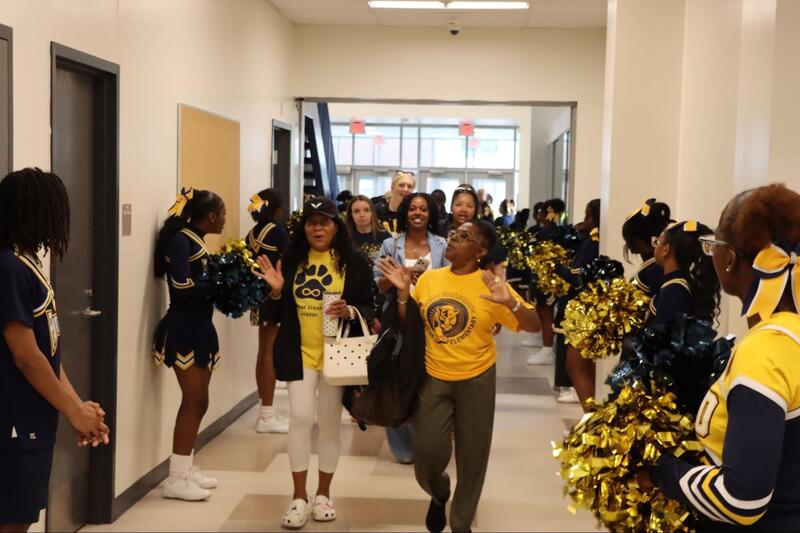 Teachers walk into the High School wearing blue and gold. The EHS Cheer team lines the hallway wearing their uniforms and carrying pompoms.