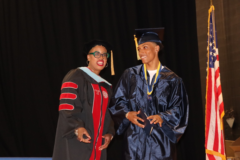 A graduate smiling after receiving his diploma from Dr. Hayes.