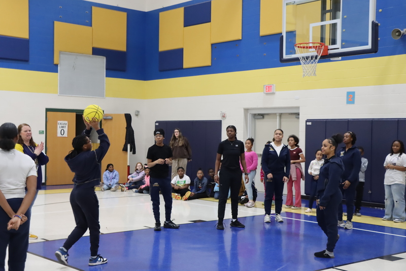 Students shooting foul shots while the high school athletes gather rebounds and cheer them on.