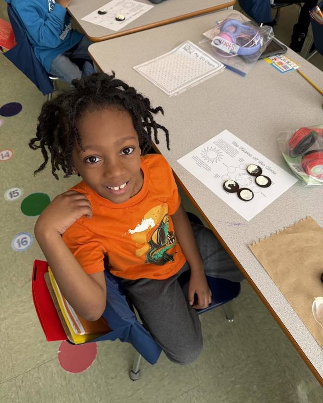 A student smiles at his desk while completing a hands-on activity modeling the phases of the moon using chocolate sandwich cookies.