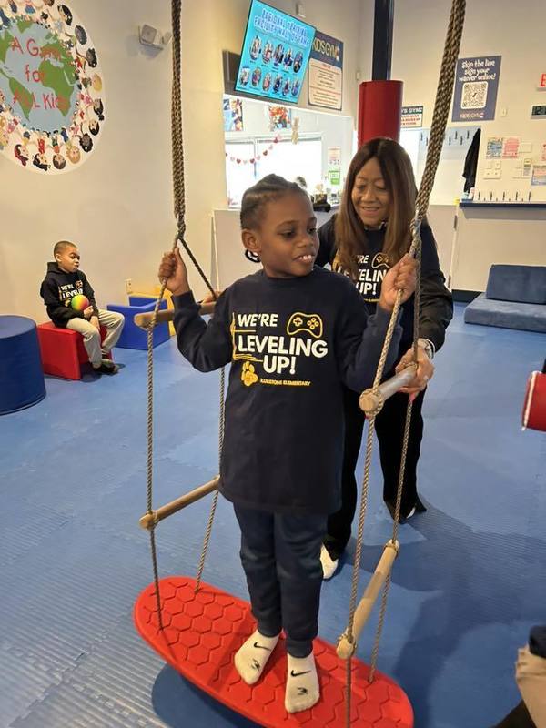 A Bluestone student plays on a hanging footboard while being assisted by a Bluestone staff member.