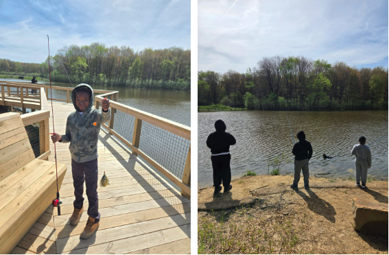 Students participate in an outdoor fishing activity, with one student proudly displaying a caught fish on a dock while others cast lines along the lake’s edge, surrounded by trees and water.