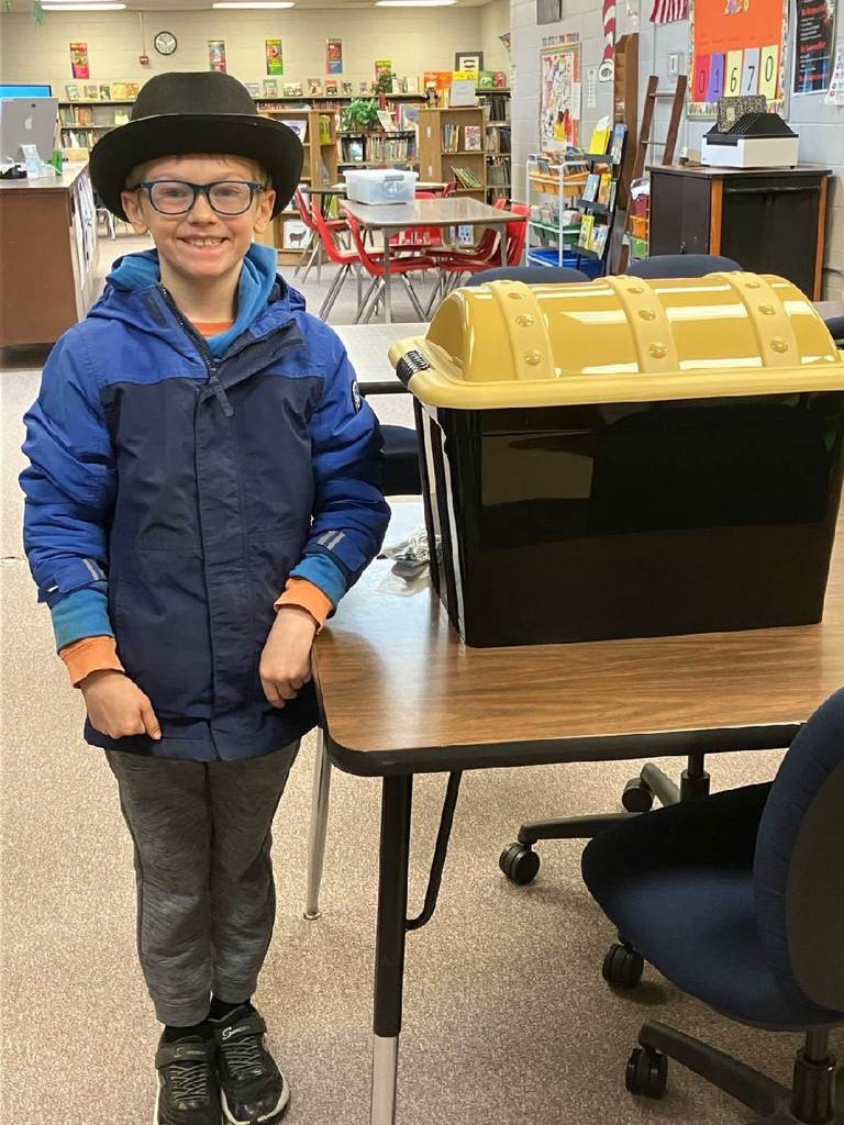 Student in black fedora standing with big plastic treasure chest full of prizes.