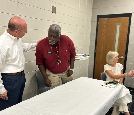 Teachers standing near and sitting at table and beginning welcome back meetings