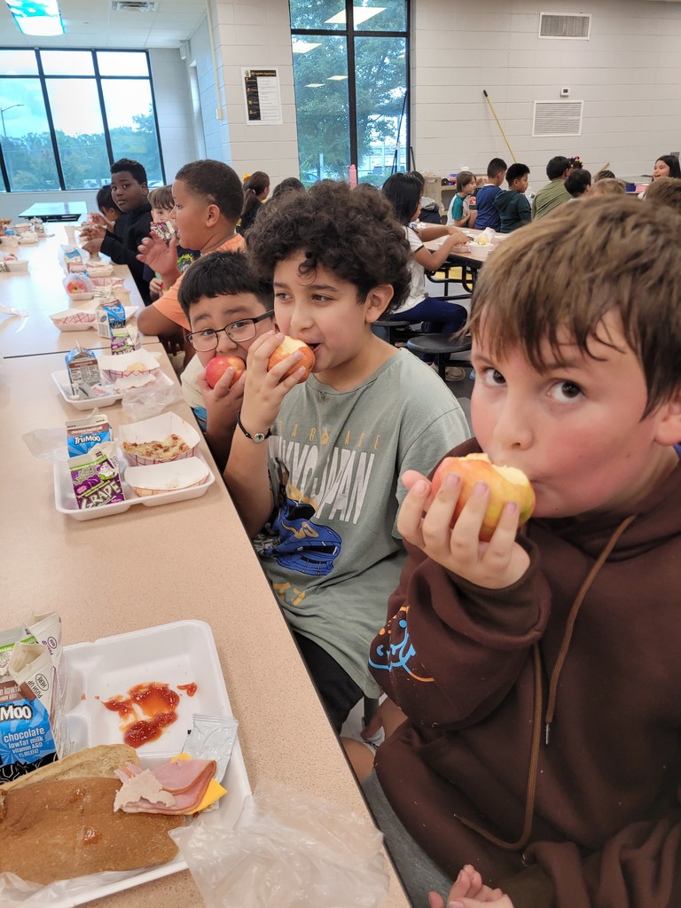 Elementary students holding apples at lunch.