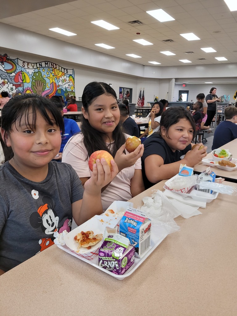 Elementary students holding apples at lunch.