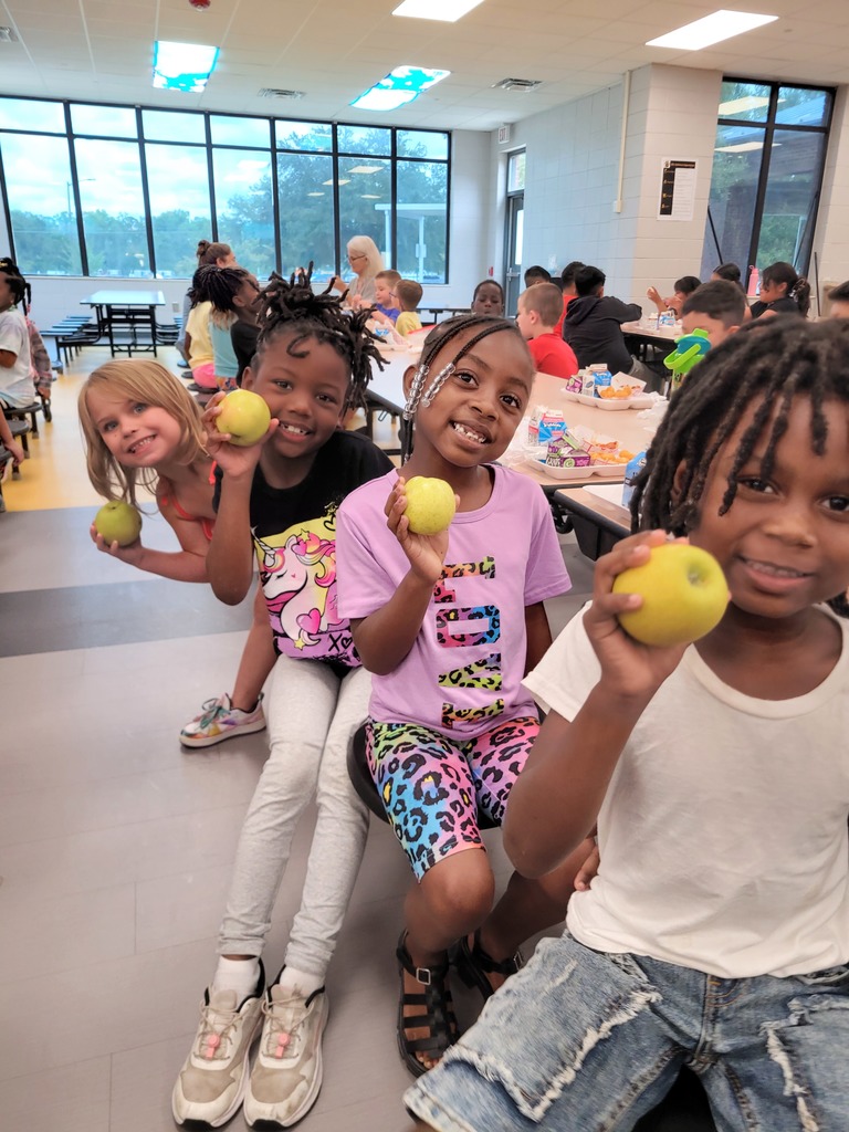 Elementary students holding apples at lunch.