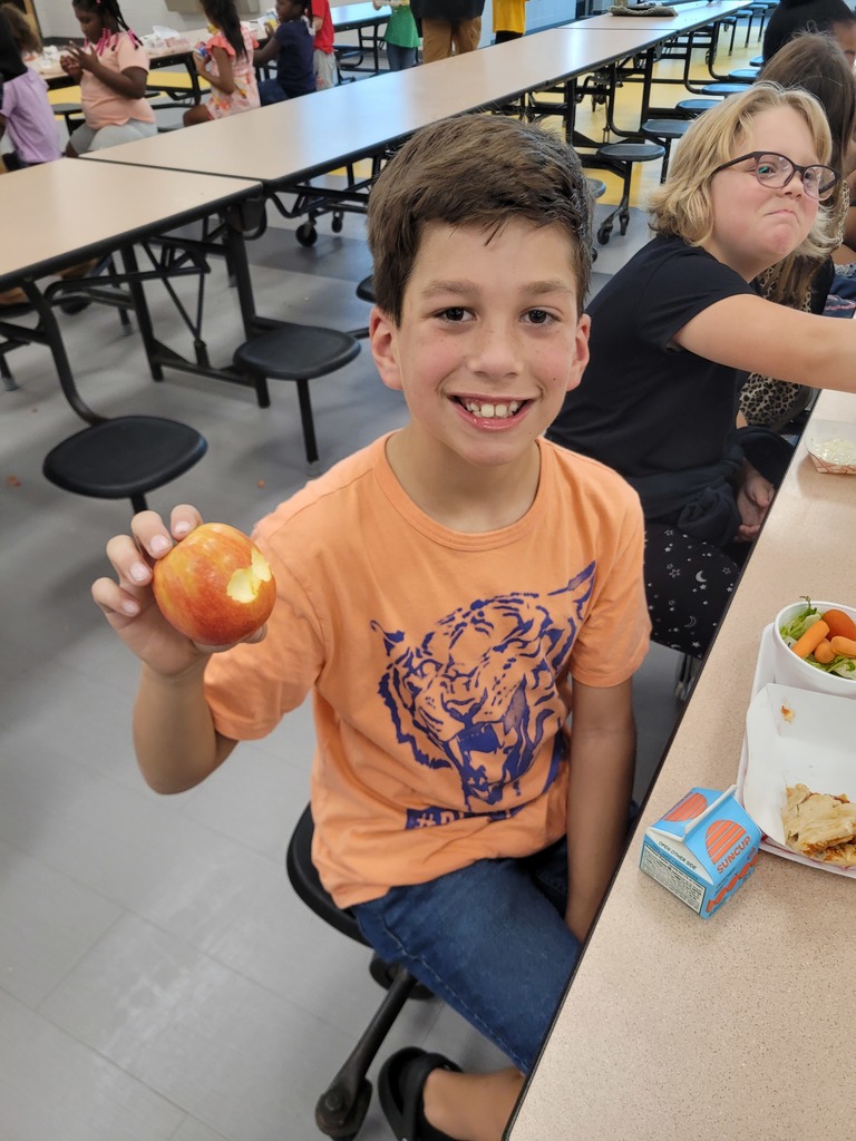 Elementary student holding an apple at lunch.