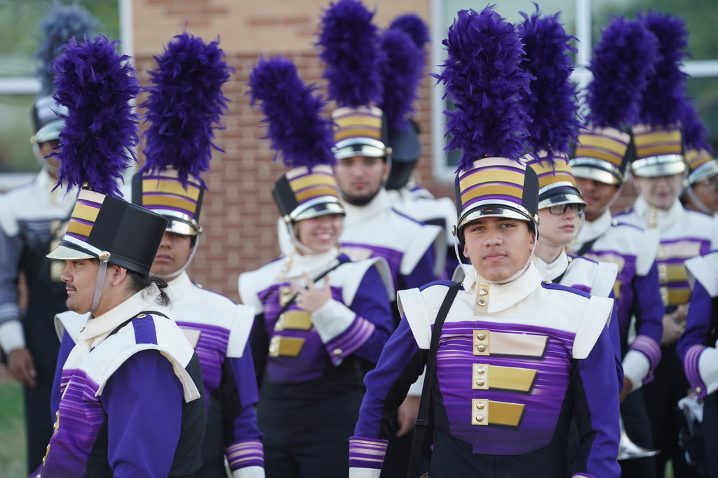 Group of students in purple and white uniforms with matching hats and boots walking in a line.