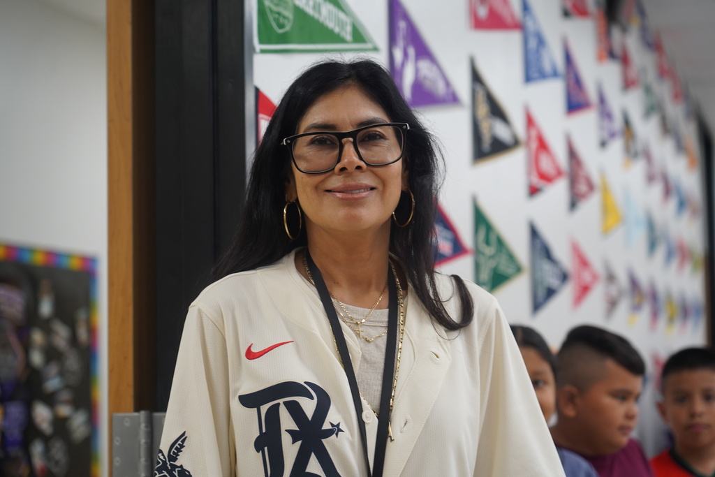 A woman with glasses smiles while standing in front of a wall with colorful triangles.