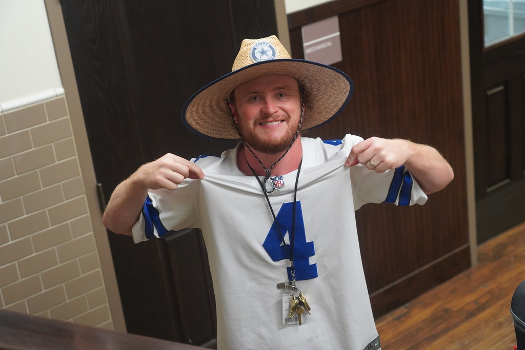 Person in a cowboy hat holds a sports jersey with the number 4, standing in front of a door.