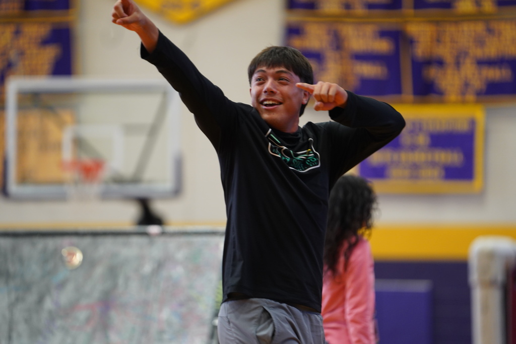 A young boy points at a basketball hoop while another person stands behind him.