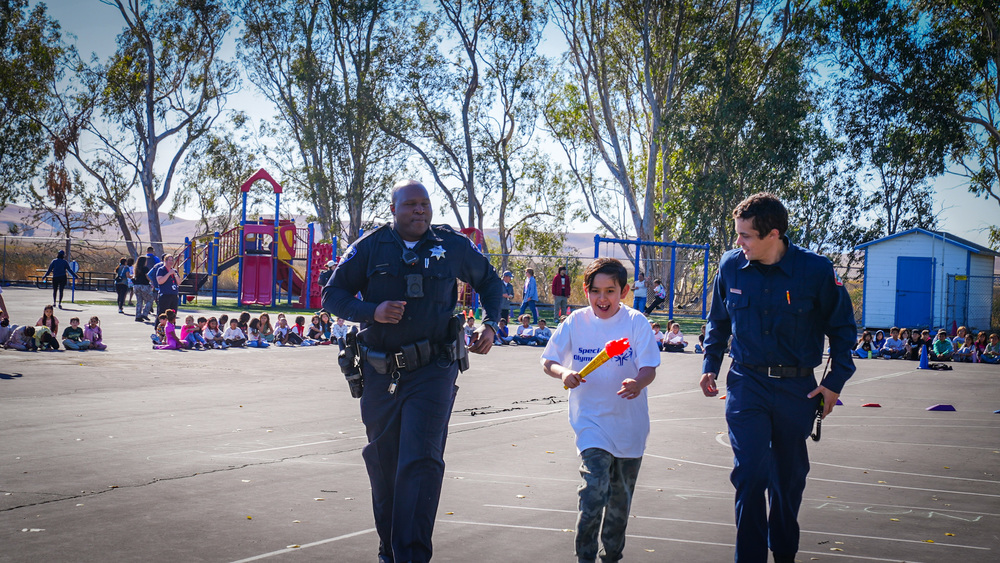 Two police officer running with an adapted PE student with the fire torch during the Adapted PE Special Olympics