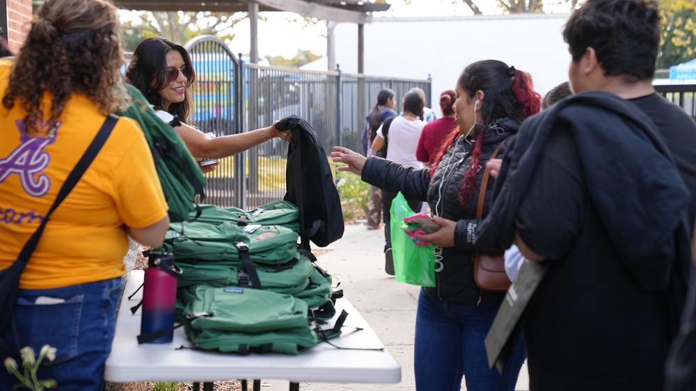fsUSD admin handing a backpack to a community member and their high school student at the Back to school Resource fair