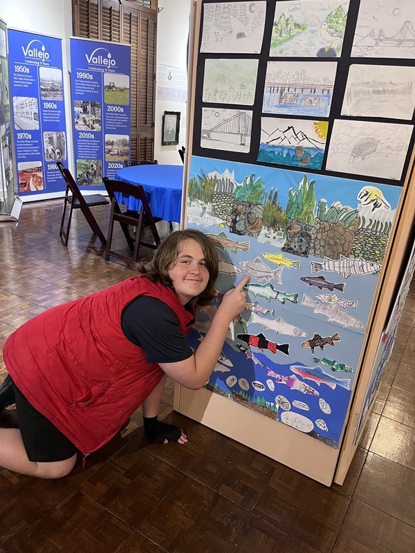 A student smiling in front of his art exhibit