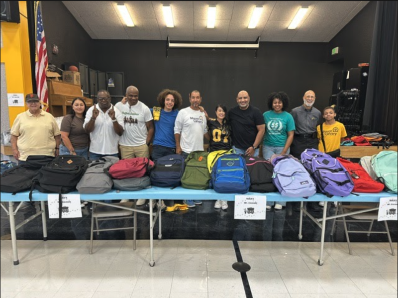 A group of staff at Sheldon Academy pose in front of a table filled with backpacks
