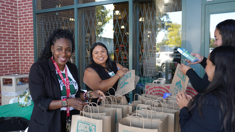 Four women from Student Support Services Department smile while stuffing bags from Dicks Sporting Goods for Shop with a Cop day.