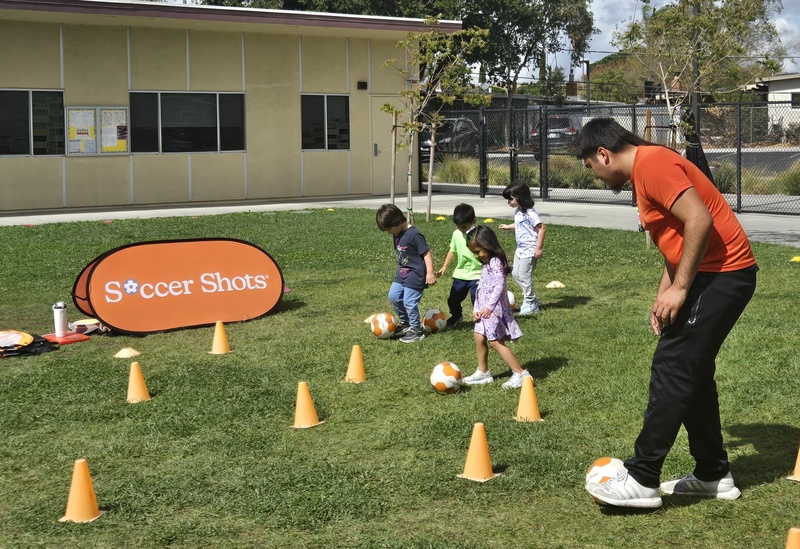 Little preschool children kicking the soccer ball through some cones.