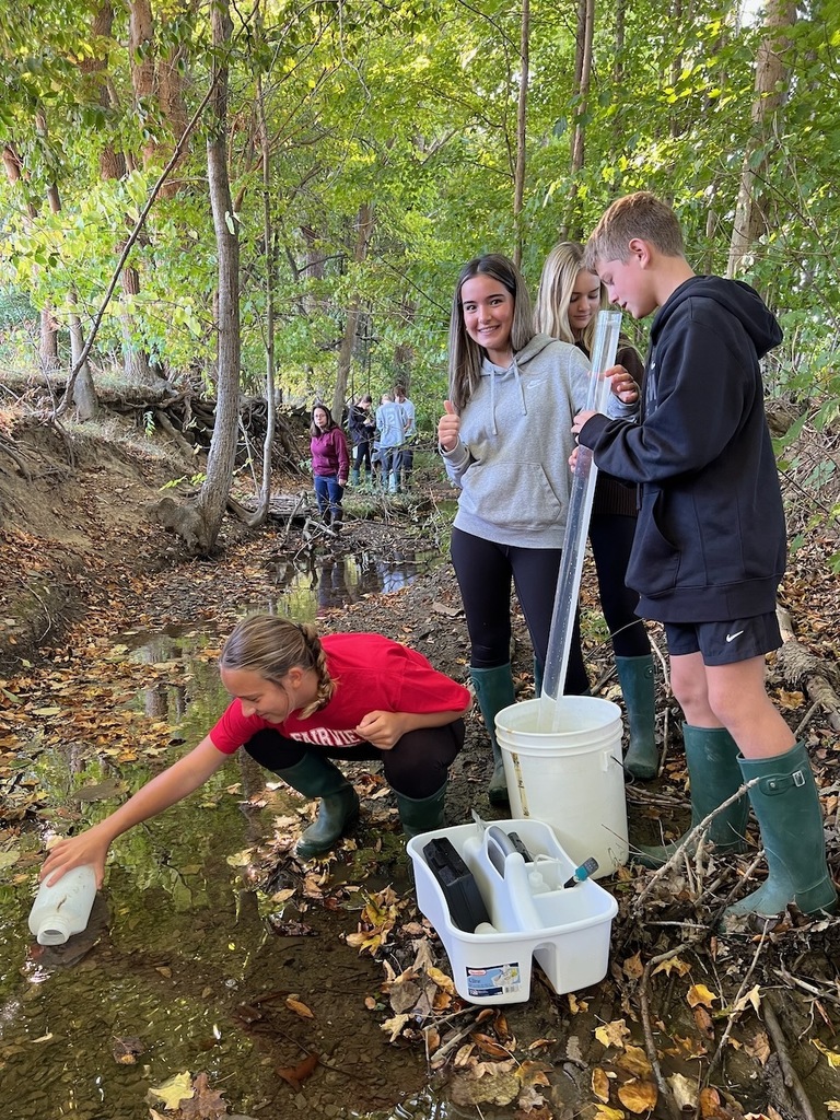 4 students filling up a container with creek water