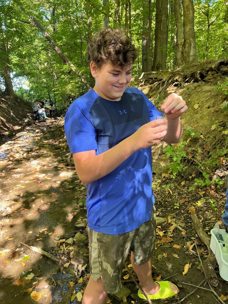 student in woods holding a beaker of water