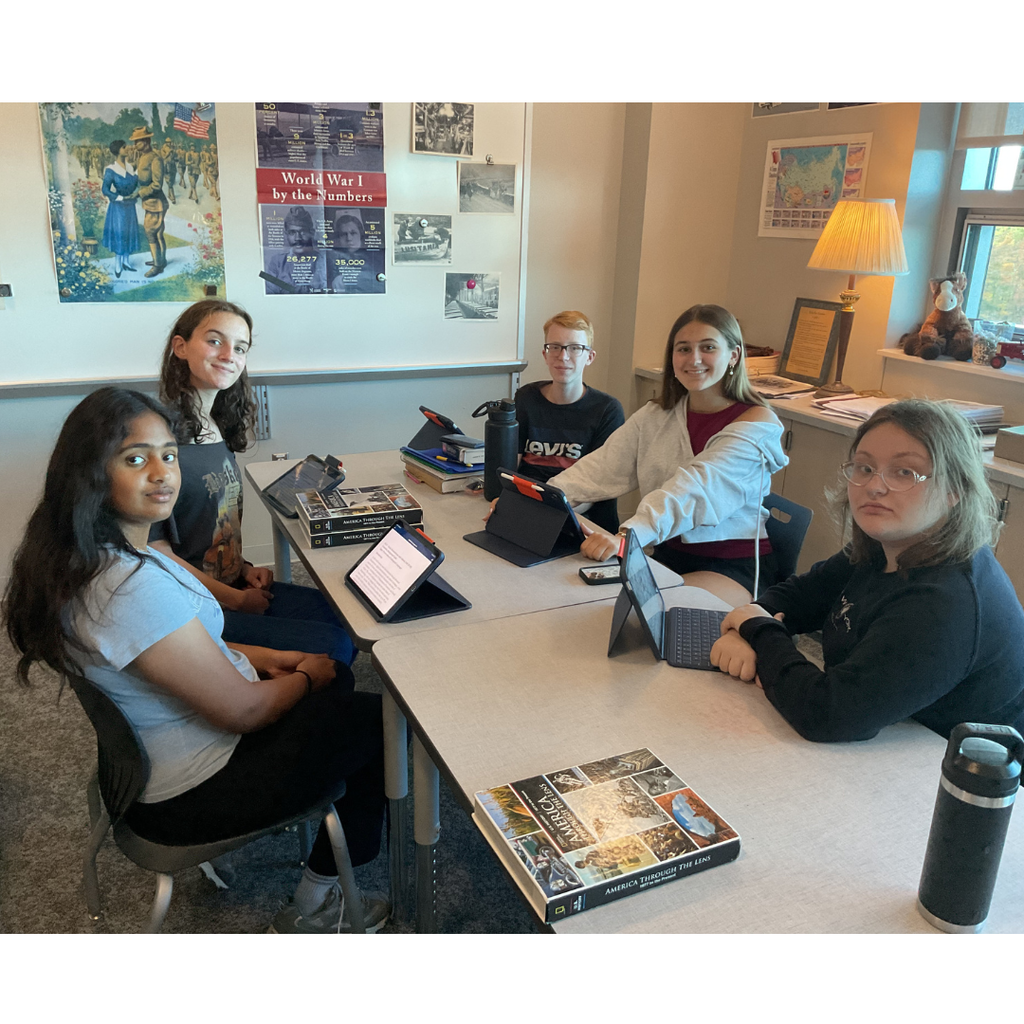 5 students sitting at a table with ipads in front of them