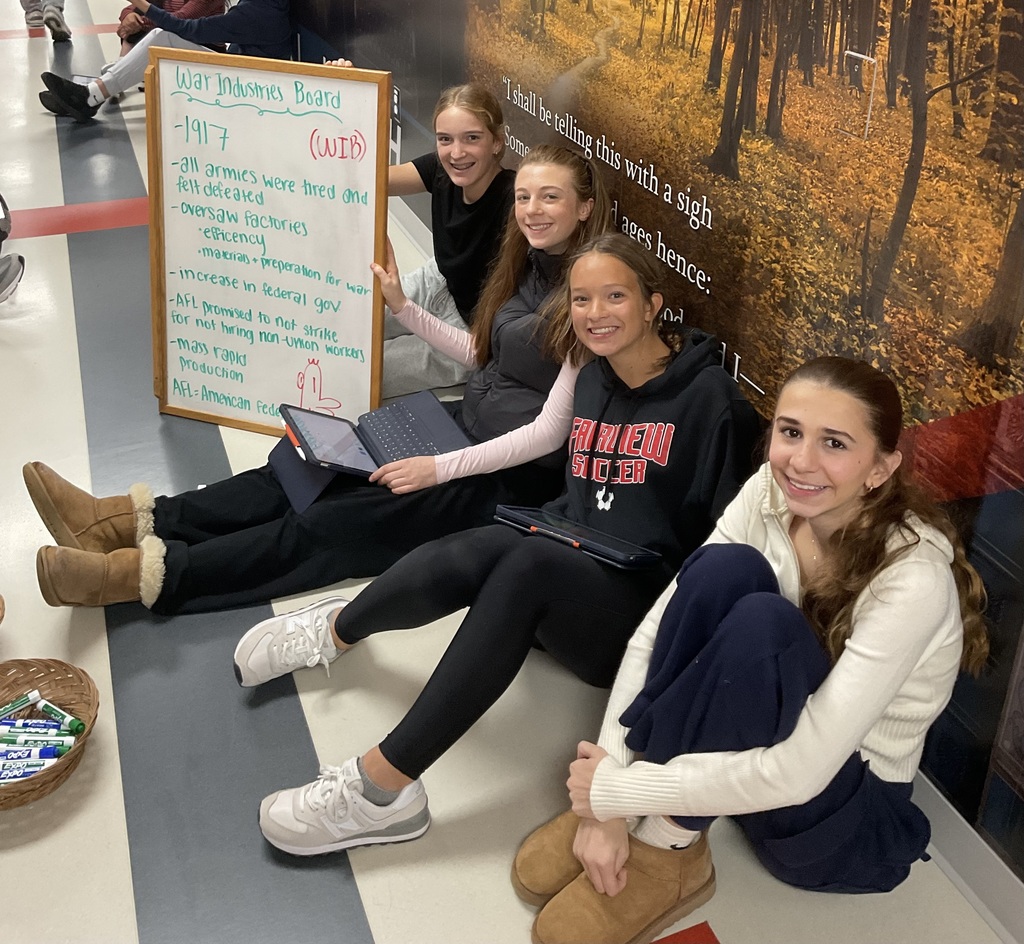 4 students holding a board about war industries