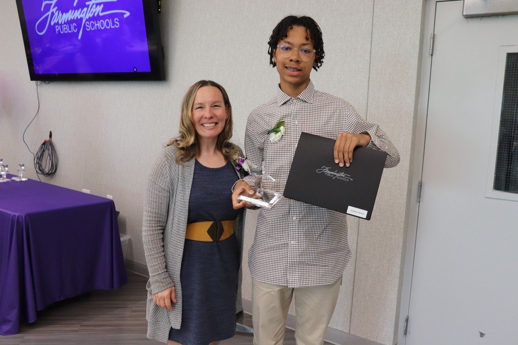 Female staff member poses for a photo with male student holding up his award.