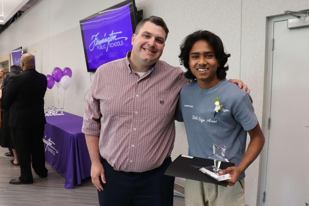 Male student holds his award and poses for a photo with a male staff member.