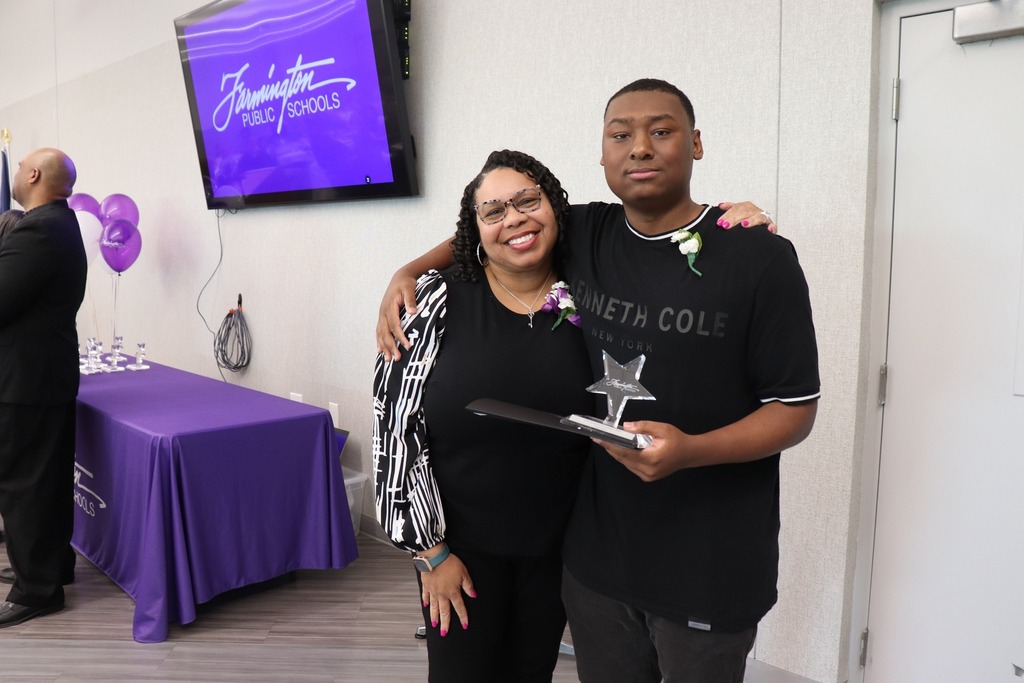 Male student holds his award in one hand and has his arm around the shoulders of a woman posing with him.