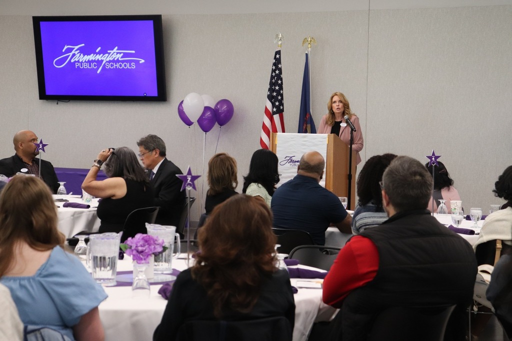 Dr. Kelly Coffin speaks at a podium in front of a banquet room full of staff and students.
