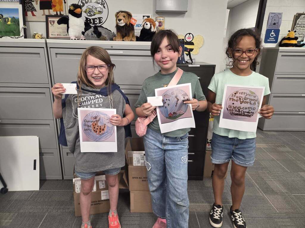 Three female students stand proudly with their award-winning artwork.