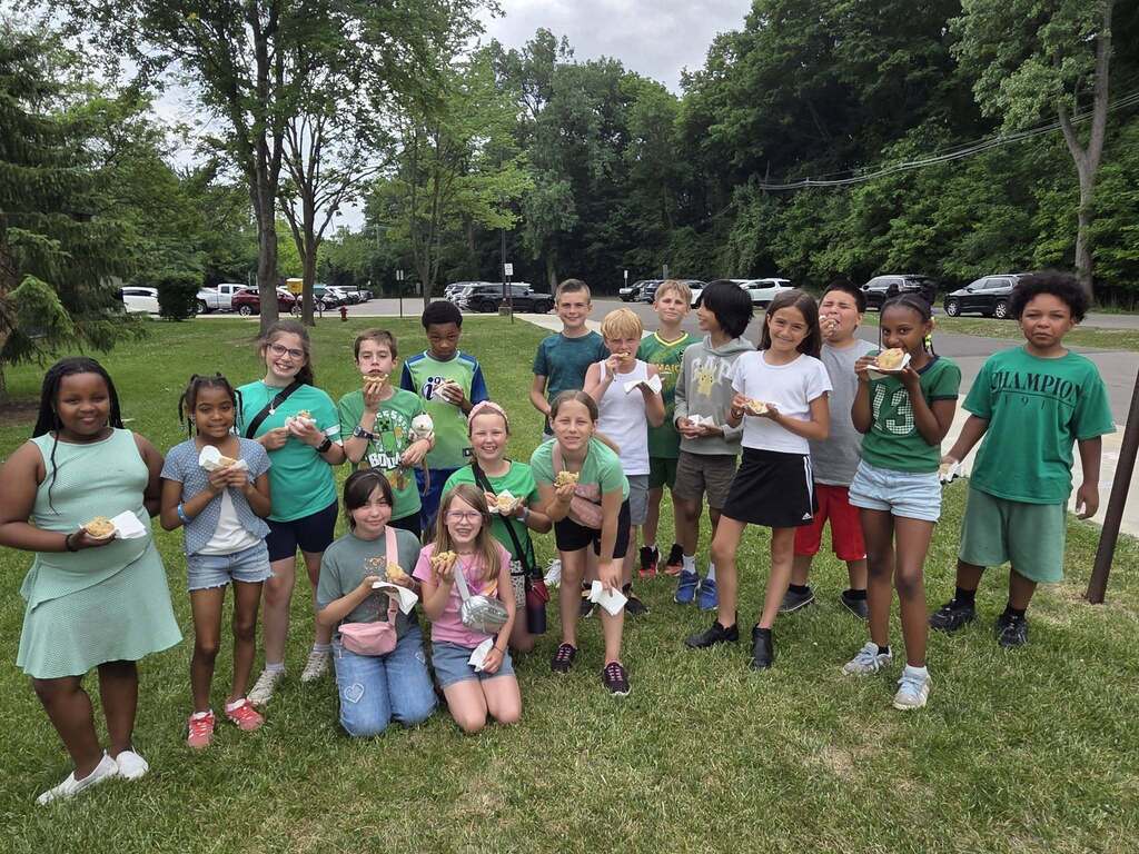 Class of students enjoys their cookie snack outside in the grassy area.