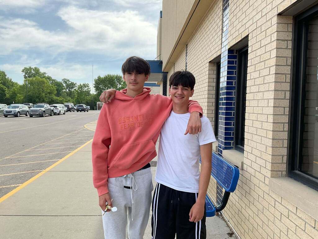 East Middle student boys stand outside the building, arm in arm, smiling.