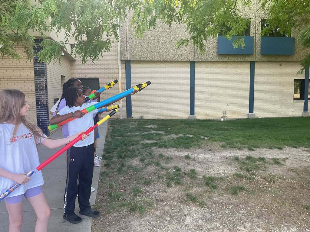 East Middle students line up outside along the sidewalk pointing foam rockets in the air preparing to launch.