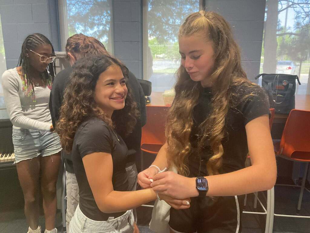 Two middle school girls help each other put on bracelets.