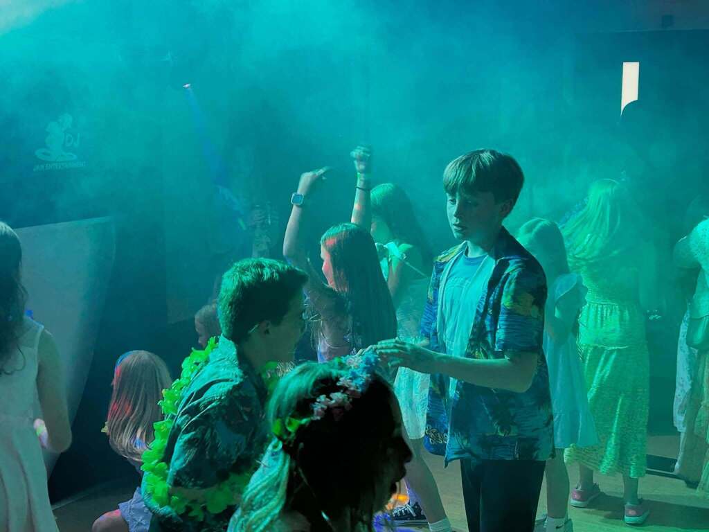 Group of children dancing and enjoying a party in a dimly lit room filled with colorful smoke effects.