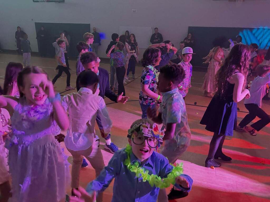 Children dancing energetically in a gymnasium with colorful lighting and festive attire.
