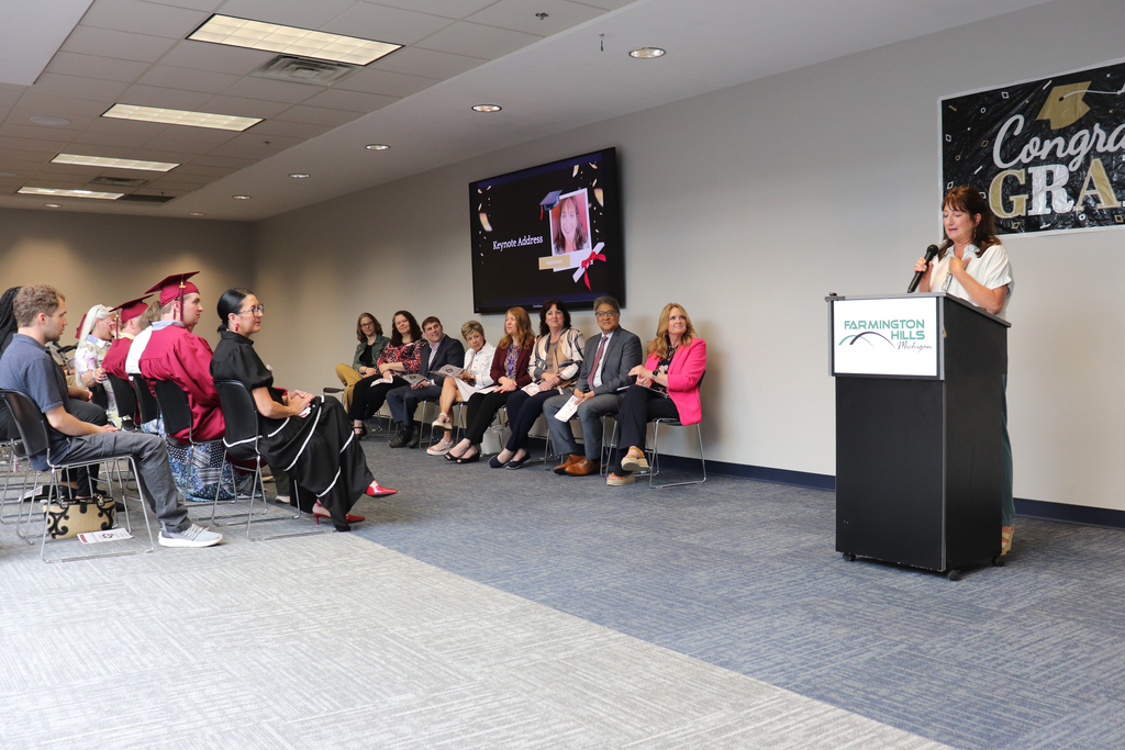 Woman at a podium speaking to a crowd of students at staff at a graduation ceremony.