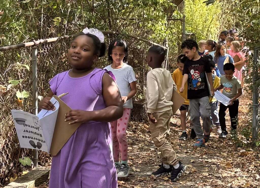 Students walking on a path outside holding notebooks and pencils.