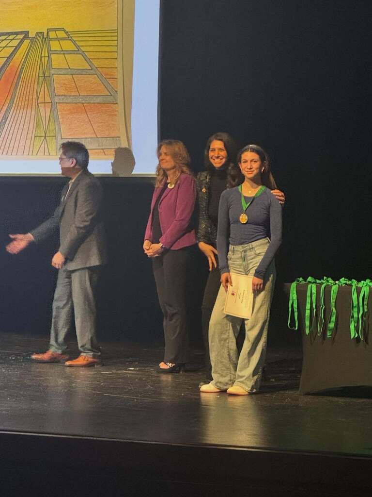 Student winner holding certificate on stage with faculty.